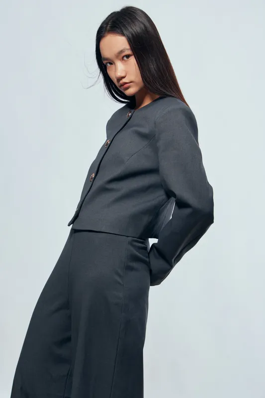 Young woman posing in gray outfit with long hair against plain background. Fashion model wearing stylish top and wide pants in studio setting for editorial or lookbook.