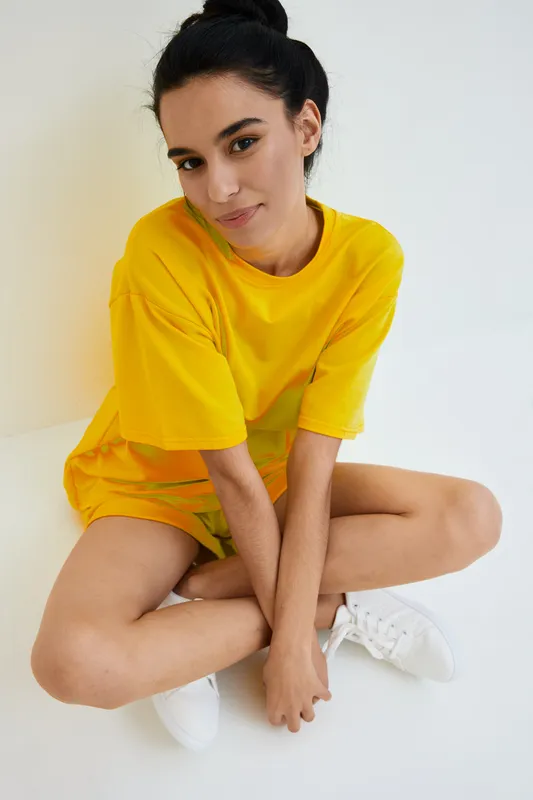 young woman in bright yellow outfit sitting cross-legged on white floor, casual style with natural light and relaxed expression