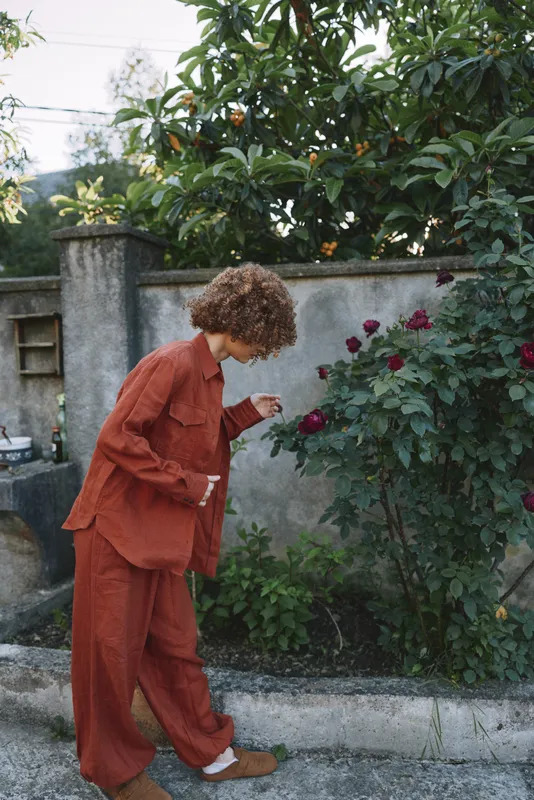 Cheerful woman lifestyle outdoors, wearing an orange suit, strolling beside a rose garden, soft sunlight, casual movement, vibrant colors, candid moment, natural setting