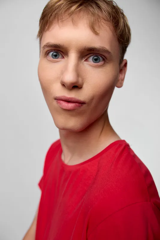 Closeup, male, young, red shirt, studio, expression, headshot with focused gaze for fashion and lifestyle use, clean background highlights skin texture, calm confidence, and approachable style