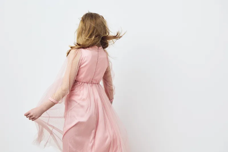 Young girl in a flowing pink dress twirling with joy against a minimalist white background, emphasizing feelings of freedom and innocence