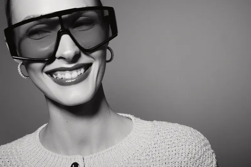 Smiling Caucasian woman with pale skin wearing large glasses and knitted sweater in black and white studio portrait. Concept of fashion, eyewear, and happiness.