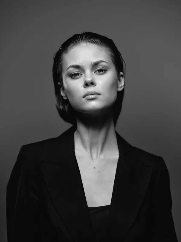 Black and white portrait of a serious woman in a blazer with a neutral gray background and confident expression