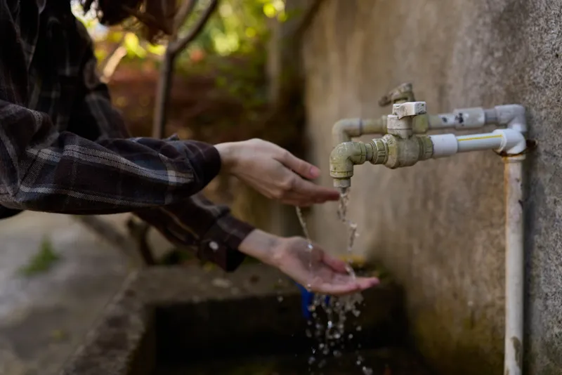Outdoor hand washing moment, a woman lifestyle scene with hands under running water from a faucet, droplets splash, casual sleeve, simple cleansing ritual