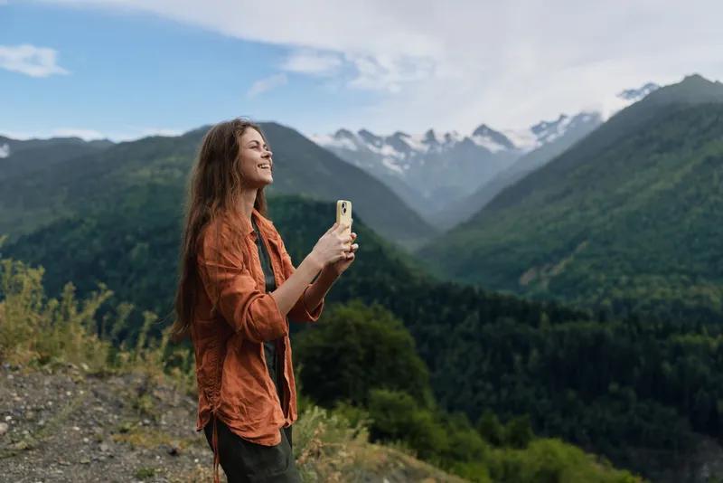 Woman hiking in mountains with smartphone capturing landscape, authenticity inclusivity, adventure and nature enjoyment