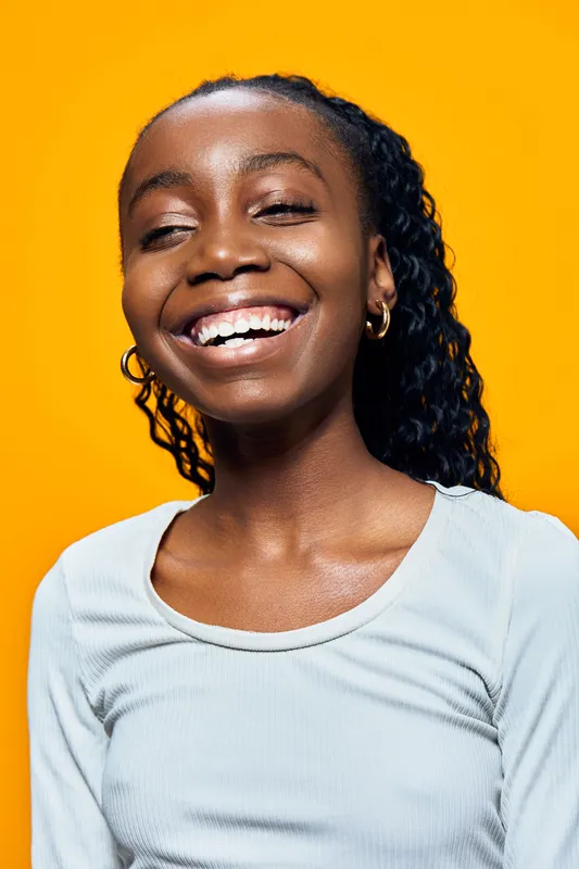 Smiling young African woman in a light shirt against a vibrant yellow background, showcasing joy and positivity in a modern, seasonal portrait