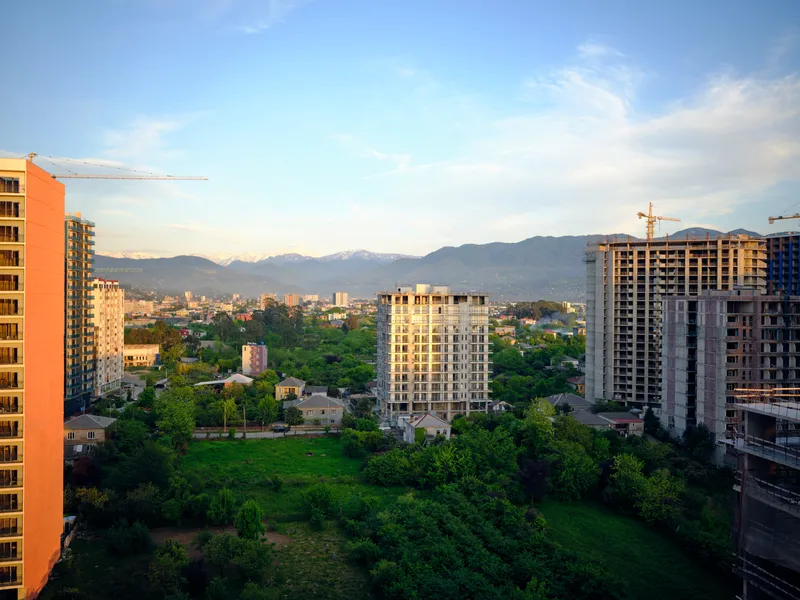 City skyline with construction cranes and new buildings surrounded by greenery and distant mountains, urban development and residential highrises in golden sunset light over the neighborhood.