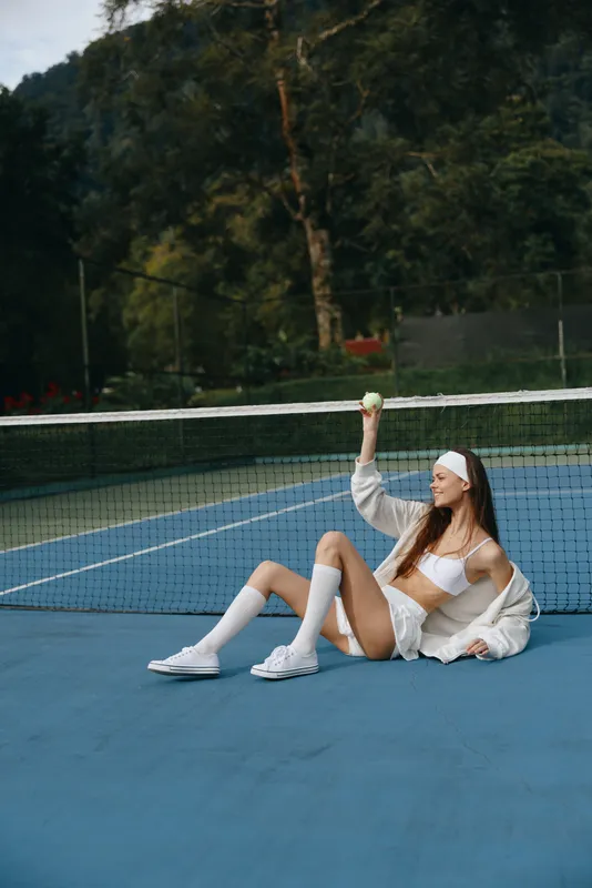 Stylish tennis player relaxing on the court, wearing sportswear and showing a confident smile under the summer sun