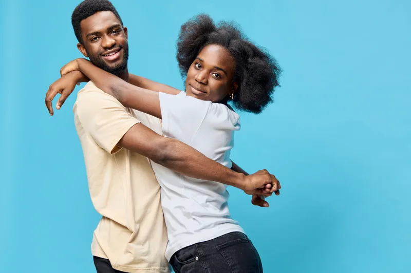 Young Black couple joyfully embracing against a vibrant blue background, showcasing love and connection in casual outfits, capturing warmth and happiness