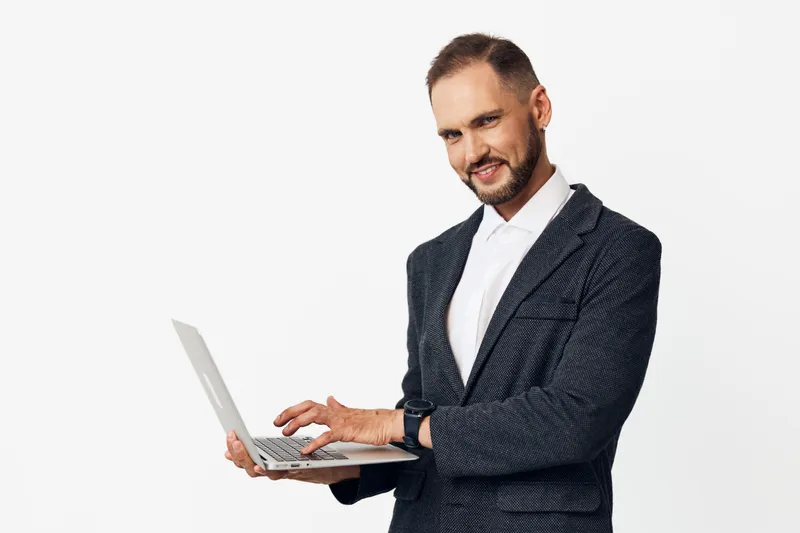 Professional male business figure with a laptop, displaying confident focus and determined emotion against an isolated bright white background for corporate use and media presentation purposes.