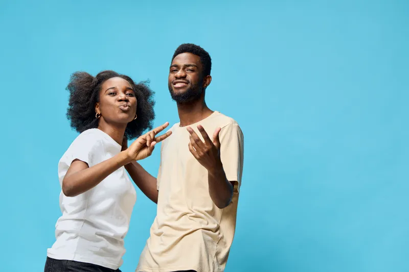Joyful young couple having fun together against a blue background, showcasing happiness and friendship through playful gestures and smiling expressions
