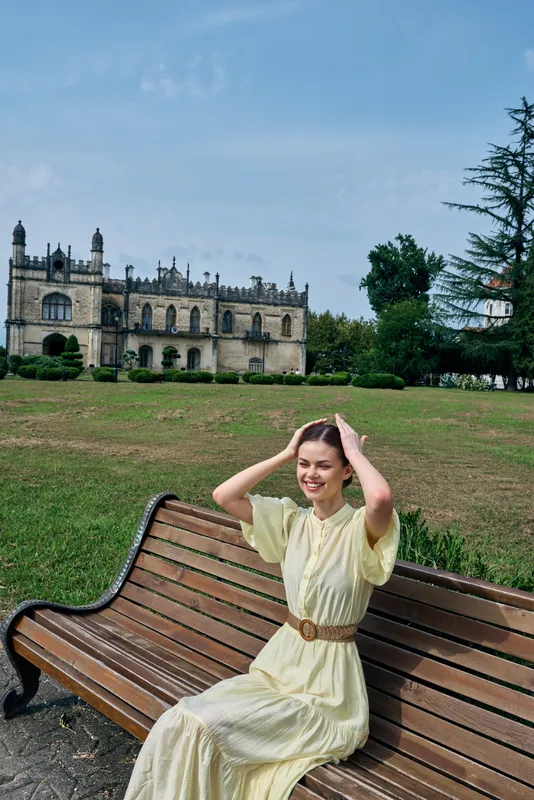 woman on bench in park with historic castle background portrait in dress smiling outdoors conveying authenticity and inclusivity