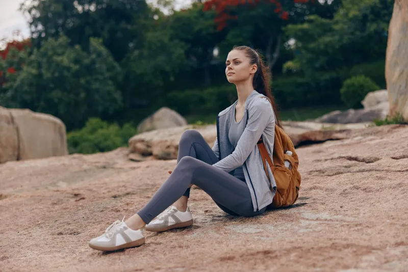 Young woman in athletic attire sitting on rocks in nature, exuding tranquility and focus, embodying fitness lifestyle and connection with nature