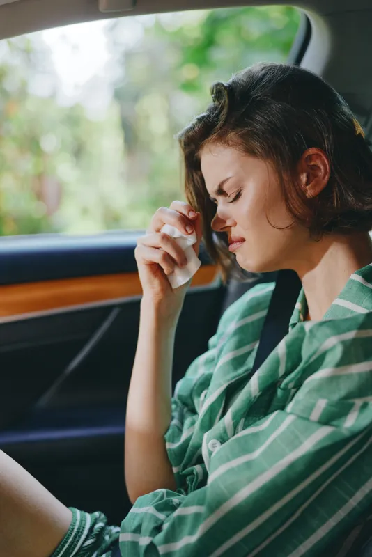 Young woman sits in a car, gently wiping a tear, capturing a moment of restraint and quiet emotion.