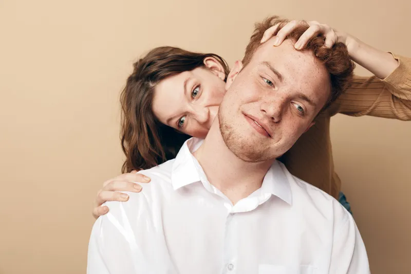 Young couple in casual clothes playfully interact with each other, woman smiling behind man with hand on his head. Concept of love, relationship, happiness, and fun moments together.
