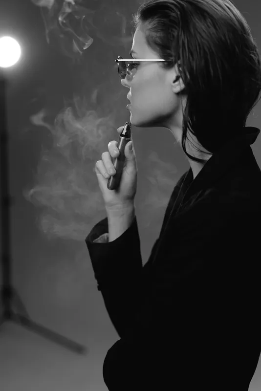 Black and white profile of a stylish woman vaping wearing sunglasses with smoke around in studio lighting