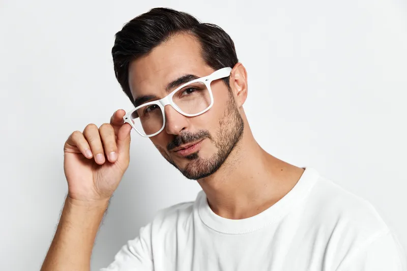 Stylish man with glasses posing confidently, showing off his trendy look in a casual white t-shirt against a plain light background. Fashion lifestyle concept.