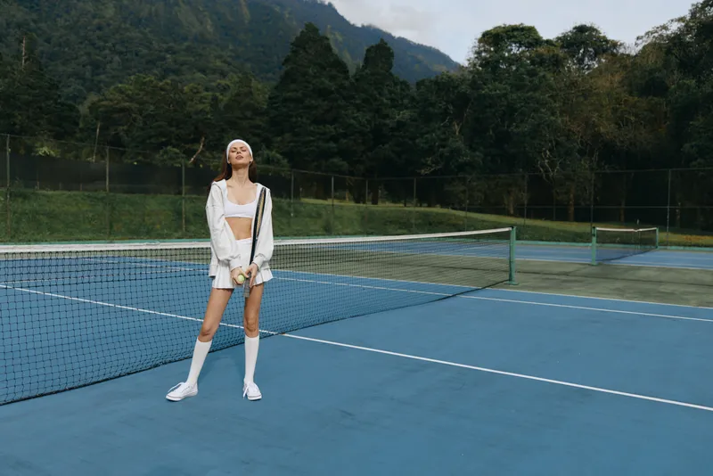 Stylish young model on a tennis court, showcasing athletic wear and a joyful expression in a lush green setting Perfect for sports and fitness themes