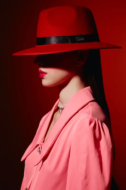 Stylish woman wearing vibrant red hat and coral pink jacket poses against red background with glossy lips and smooth skin. Beauty, fashion, and creative portrait in dramatic lighting.