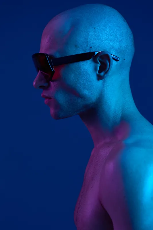 Stylish man in sunglasses against a vibrant blue background. The image features contrasting lights that create an eye-catching visual effect.