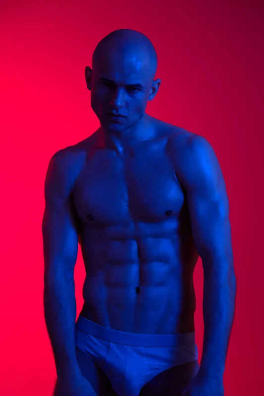 A striking blue-tinted portrait of a man showcasing strong physique and intensity. The dramatic lighting emphasizes his chiseled features and creates a bold aesthetic.