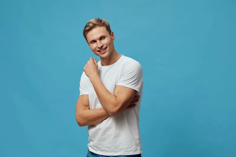 Smiling young man with short hair in casual white t-shirt posing in studio on bright blue background, cheerful expression, casual style, lifestyle concept, portrait.