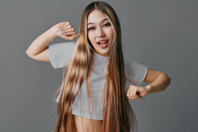 Young woman with long straight hair and casual crop top posing and smiling in studio with plain background for beauty hair care fashion and youth lifestyle concept.