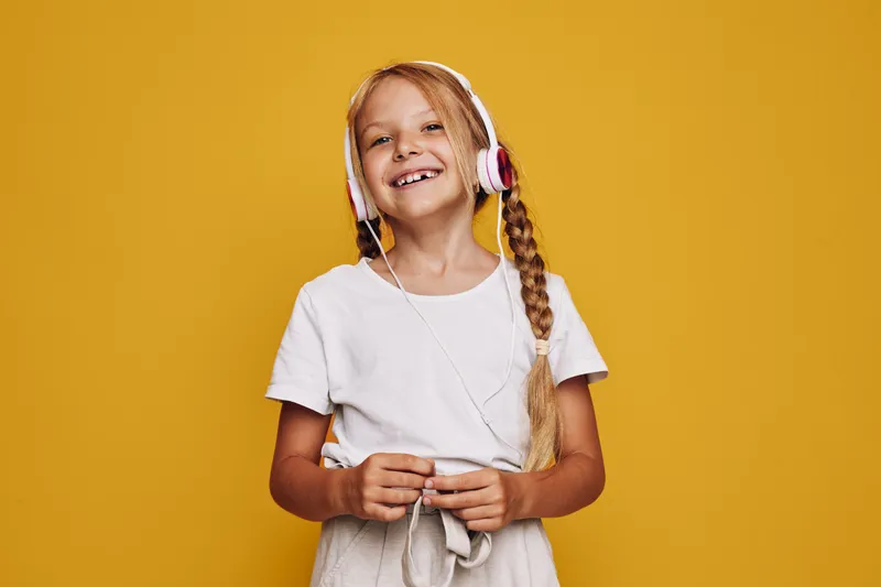 Happy girl with long braided hair wearing headphones and smiling while enjoying music. She stands against a vibrant yellow background. Concept of joy and leisure.