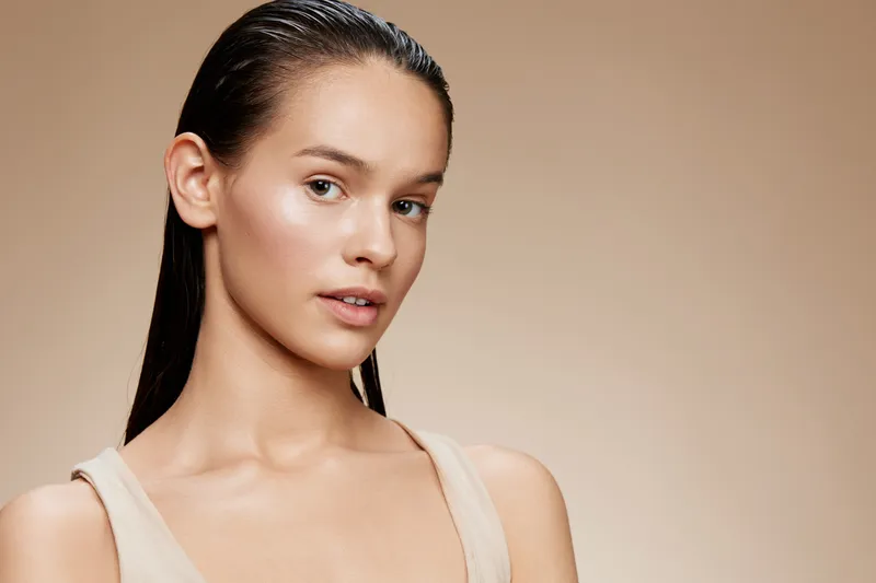 Portrait of a young woman with wet hair wearing a beige top, showcasing natural beauty and confidence against a neutral background