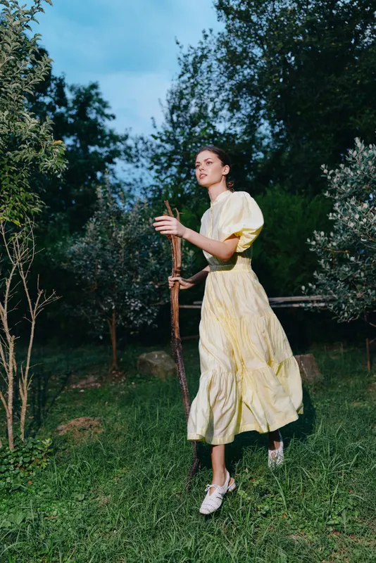 Woman in yellow dress walking in countryside, nature portrait with authenticity and inclusivity, serene outdoor scene, greenery and evening light,