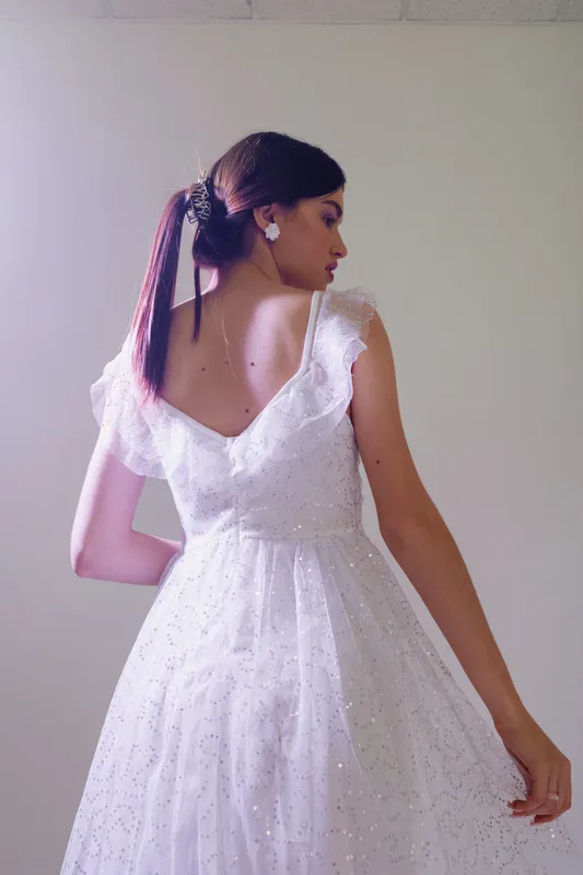 Young woman in a white elegant dress poses with her back turned. Soft lighting highlights her beauty and fashion style in a minimalistic studio setting.