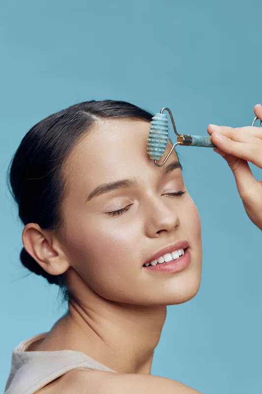 Young woman enjoying a skincare routine with a jade roller, promoting beauty and self care in a serene blue background