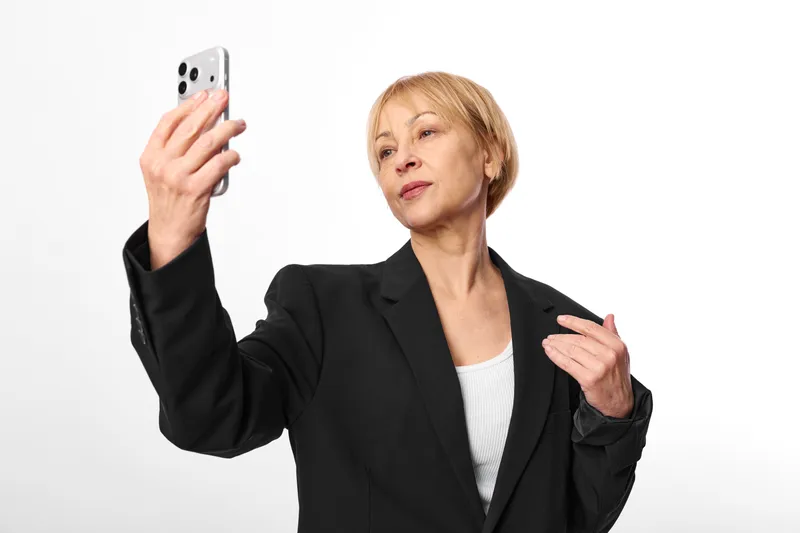Woman holding smartphone in a studio portrait on a white background, subtle hand gesture, focused expression, modern technology, communication and selfie with calm confidence.
