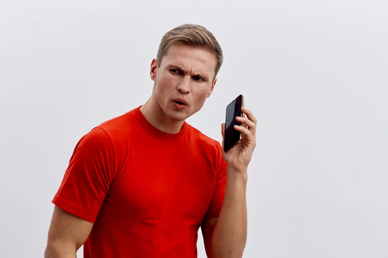 confused man holding black mobile phone in red t-shirt looking side isolated on white background cyber security concept
