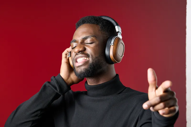 Young Black man enjoying music with headphones, expressing joy and relaxation in a cozy indoor setting with a warm red background