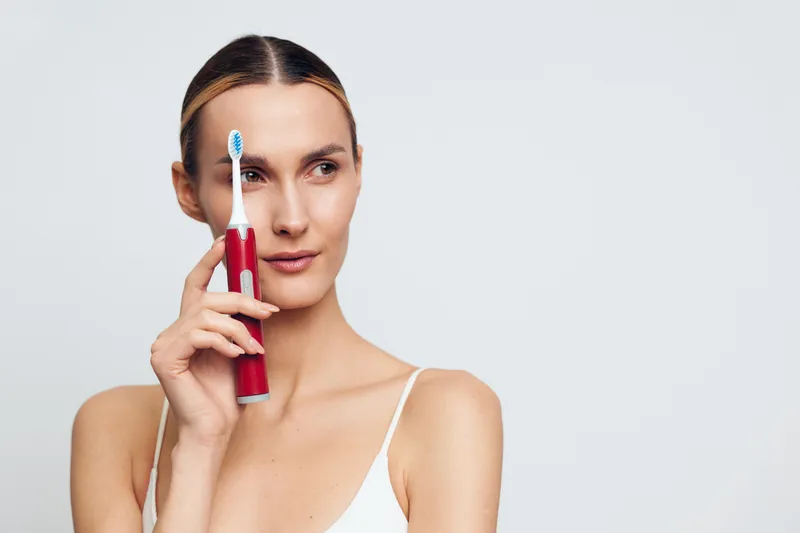 A woman holds a red toothbrush near her face, poised to brush. Bright, minimalist setting conveys daily dental care, personal hygiene, and self care routine.