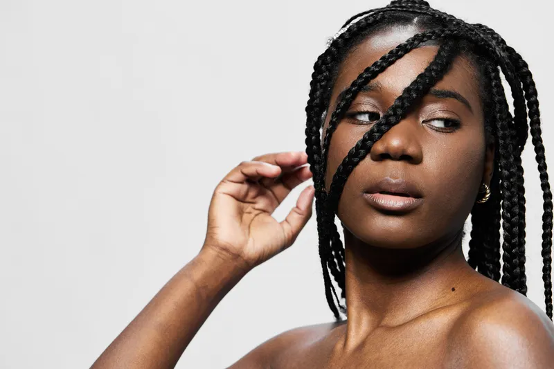 A confident young Black woman with braided hair posing against a minimalist white background, conveying strength and beauty through her expression