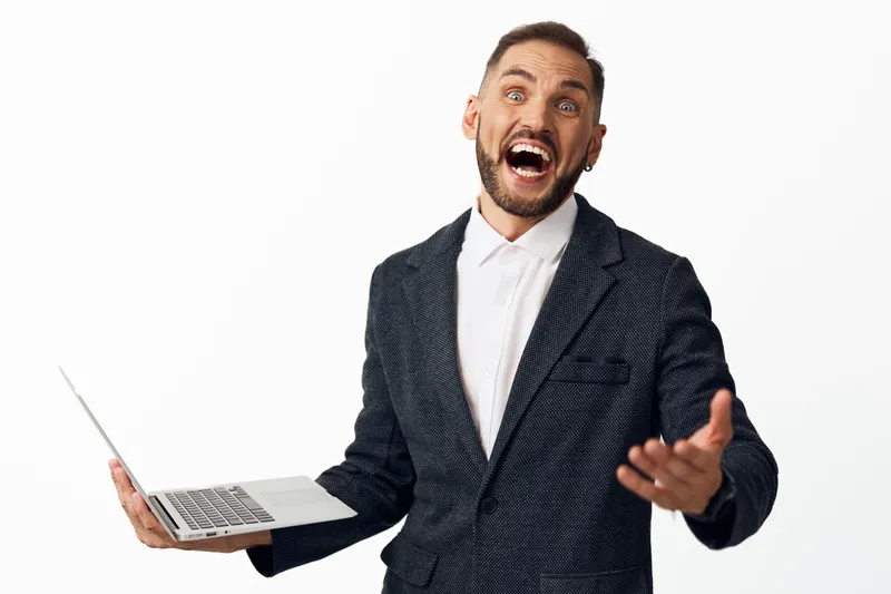 A confident business professional man holds a laptop, exuding enthusiasm against an isolated colored background; the energetic stance and open gesture convey motivation and dynamic leadership.
