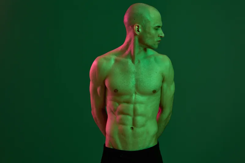 Confident man with a toned physique, showcasing strength and determination against a vibrant green backdrop. This black and white image captures dynamic energy.