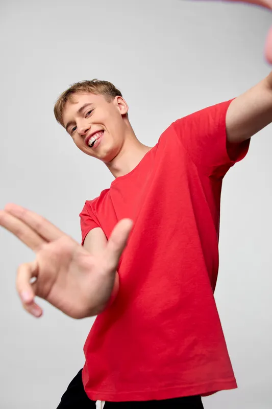 Young man in a red shirt dances with outstretched arms, exuding energy, joy and motion in a bright studio setting for dynamic lifestyle or fitness themes