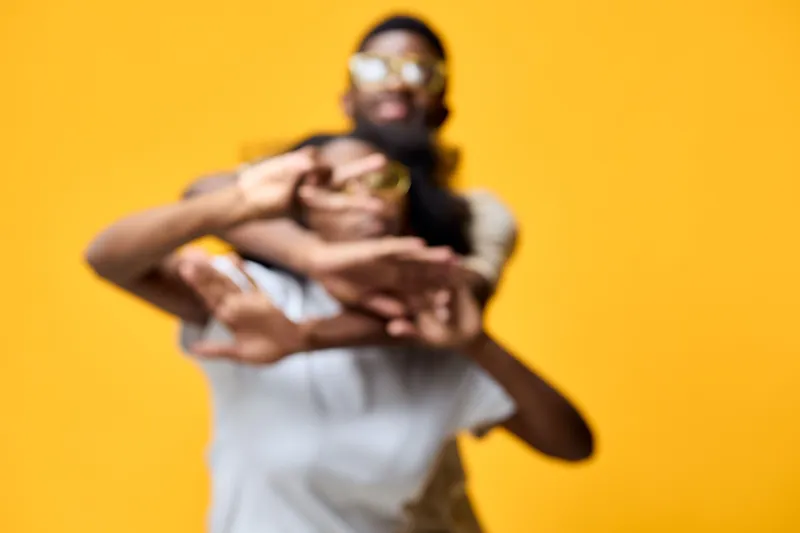 Joyful young couple playfully posing against a vibrant yellow background, showcasing summer style and fun emotions with trendy sunglasses and casual clothing