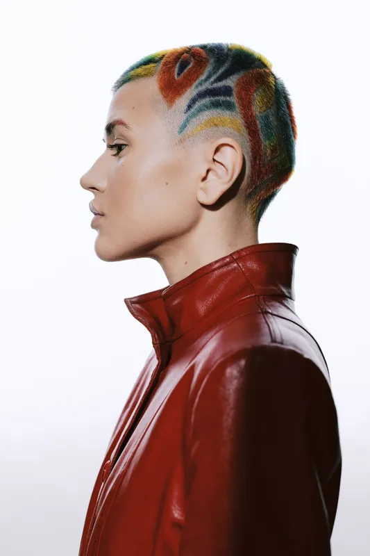 Woman with colorful short hair wearing a red leather jacket, showcasing bold style and creative self-expression with a confident side profile.