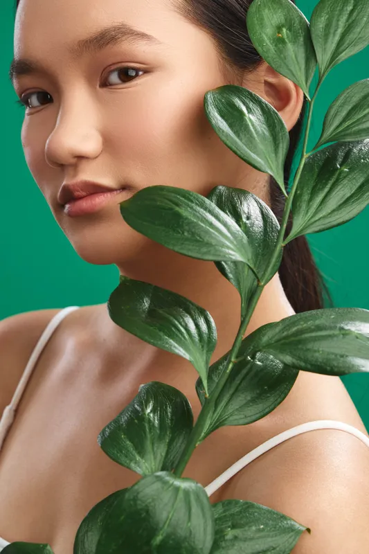 asian woman is photographed in a closeup portrait with large green leaves partially framing her face, creating a fresh, natural and stylish mood for fashion and lifestyle projects.