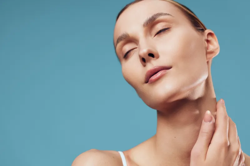 Serene closeup portrait of a woman with closed eyes, soft light, and flawless skin against a blue backdrop, conveys calm confidence, self care, and gentle relaxation