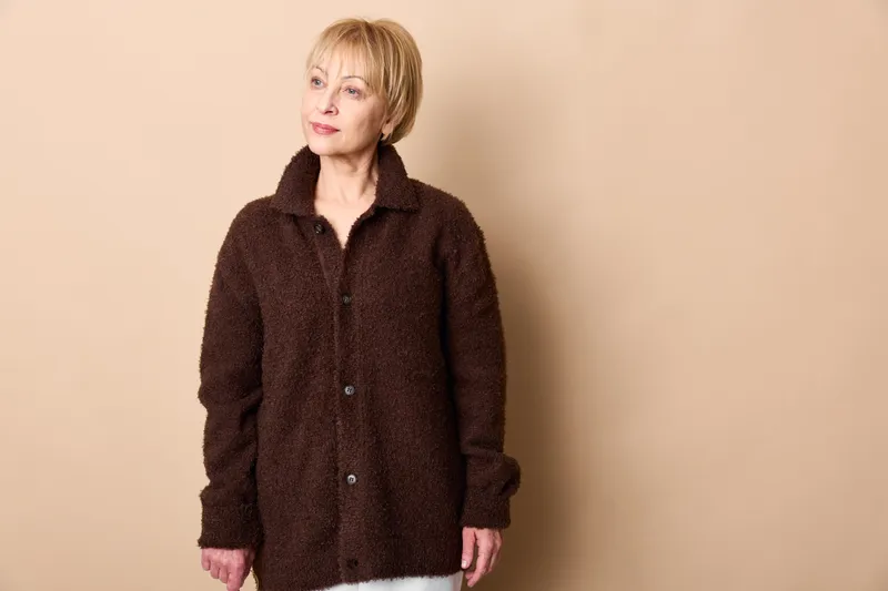 Woman portrait, blonde woman in dark sweater stands in studio light, beige background, relaxed casual fashion, soft fuzzy texture, calm face, gentle smile