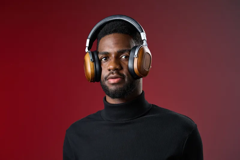 A young Black man wearing stylish headphones poses confidently against a rich red background, showcasing modern audio technology and fashion