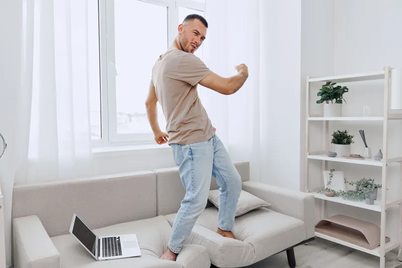 Man dancing joyfully in a cozy living room, balancing work and leisure, embracing authenticity, and promoting mental health awareness in everyday life. ###
