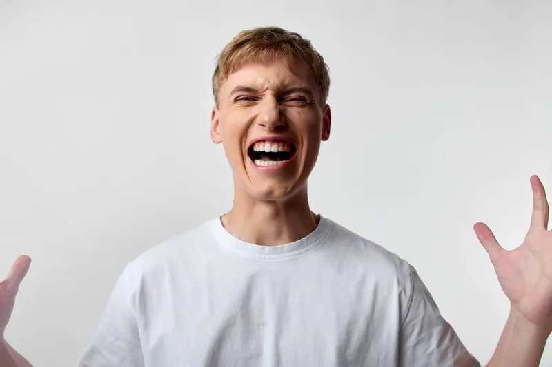 Man, scream and open mouth gesture in studio with white background, conveying high energy, excitement and intense emotion for dynamic advertising, action stock footage or expressive imagery