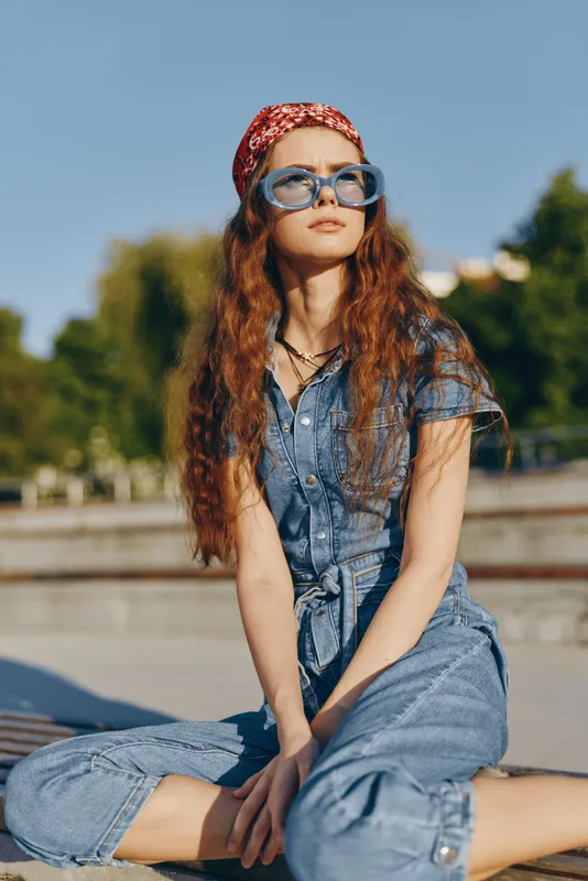 Lifestyle woman wearing modern boho-western denim street style with a red bandana and oversized glasses, captured in natural light with film color tones.