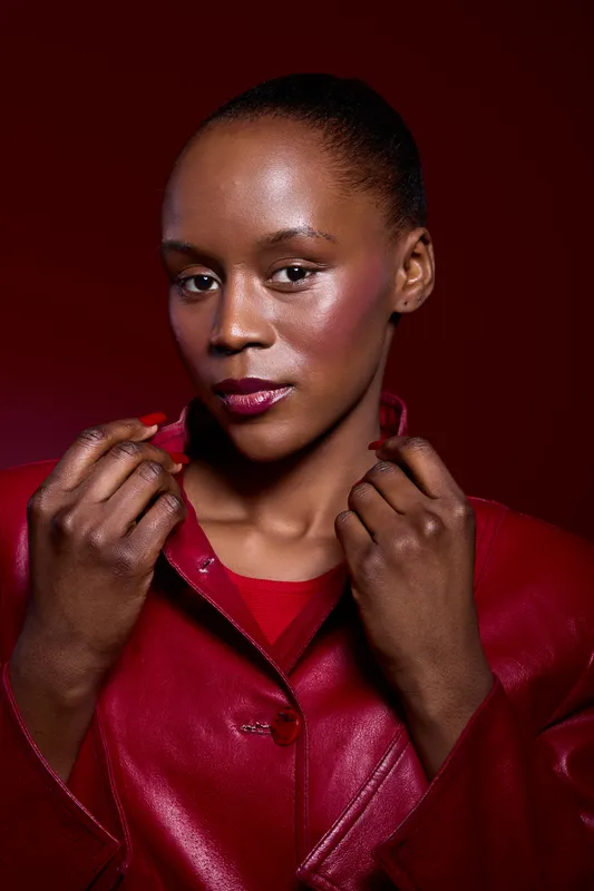Close-up portrait of a confident dark skinned African woman wearing a red leather jacket against a deep red background. Concept of fashion, beauty, and empowerment.